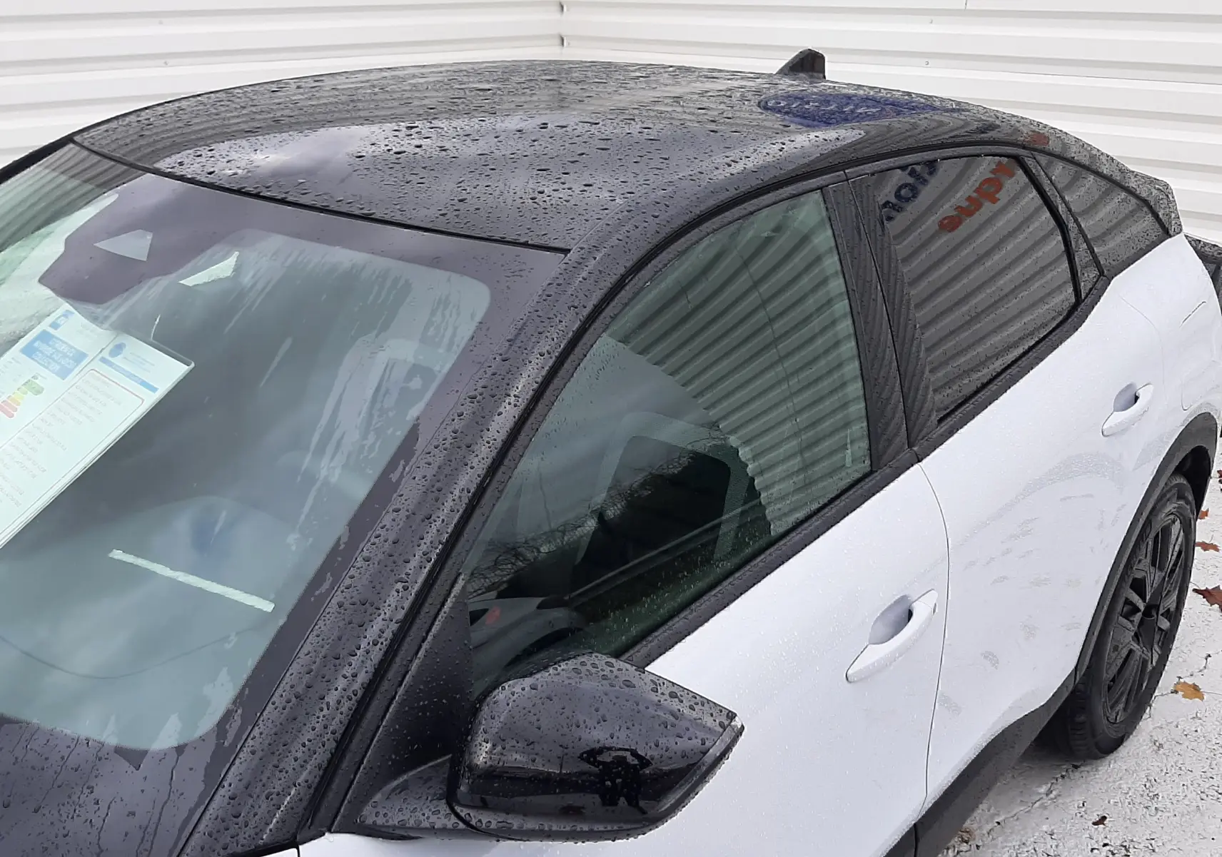 Vue 3/4 avant droit d'une Citroën C4 blanche Okenite avec toit noir Perla et rétroviseur noir brillant sous pluie fine.