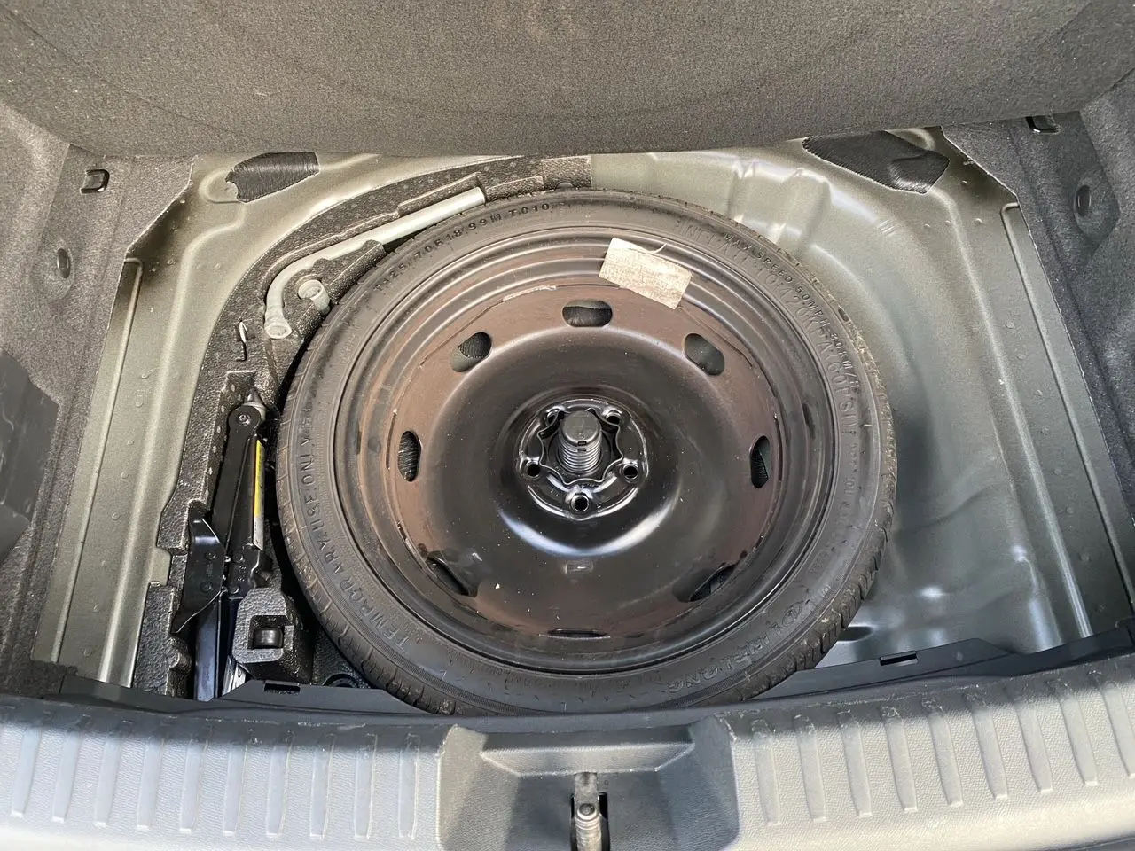 Vue plongeante sur la roue de secours noire et le cric dans le coffre d'une CUPRA Leon 2023.