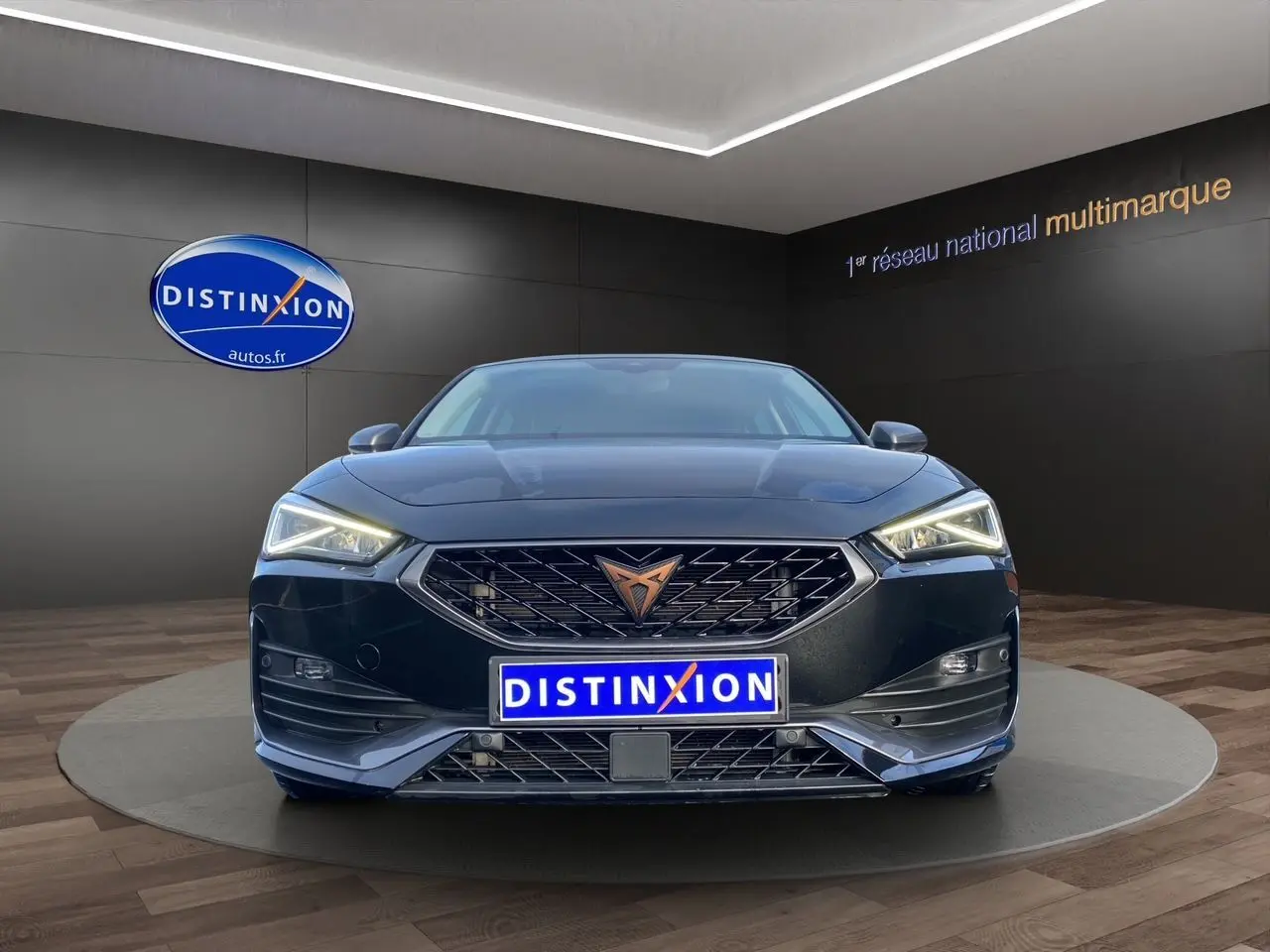 Vue avant d'une CUPRA Leon noire 2023 avec calandre distinctive et phares LED allumés dans un showroom.