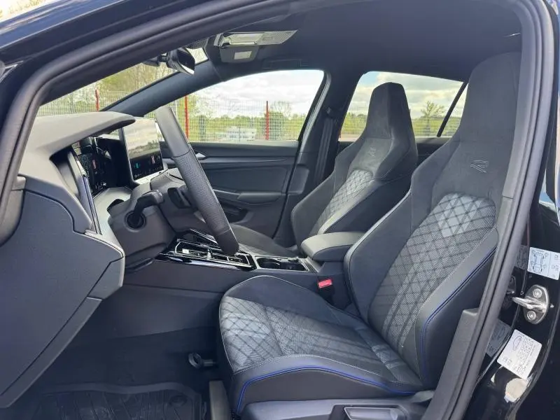 Vue intérieure côté conducteur de la Volkswagen Golf R-Line noire, sièges sport en tissu et alcantara avec surpiqûres bleues.
