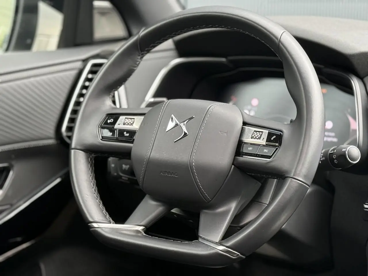 Gros plan sur le volant cuir noir du DS7 2025 avec commandes intégrées et logo DS au centre.