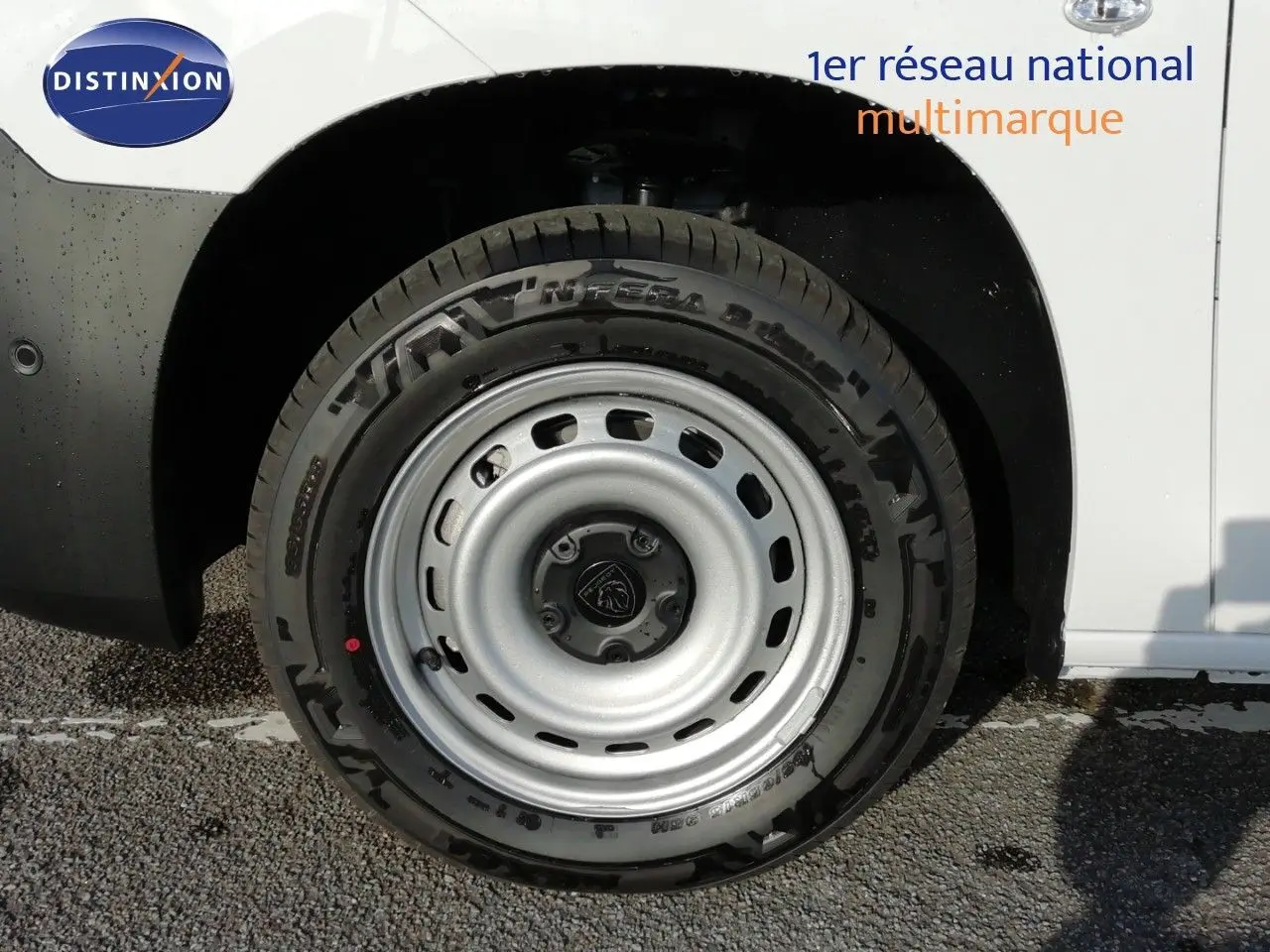 Gros plan sur la roue avant droite d’un Peugeot Partner blanc Kaolin avec jante acier et logo Peugeot au centre.