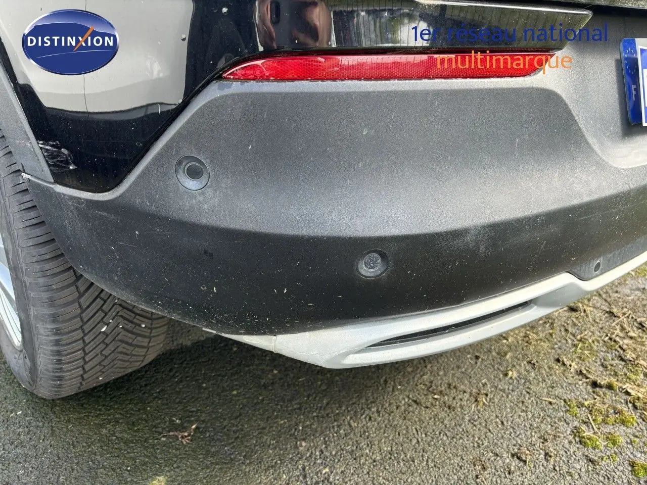 Gros plan sur le pare-chocs arrière noir d'un Opel Grandland X 2019, avec capteurs de recul visibles et feu rouge.