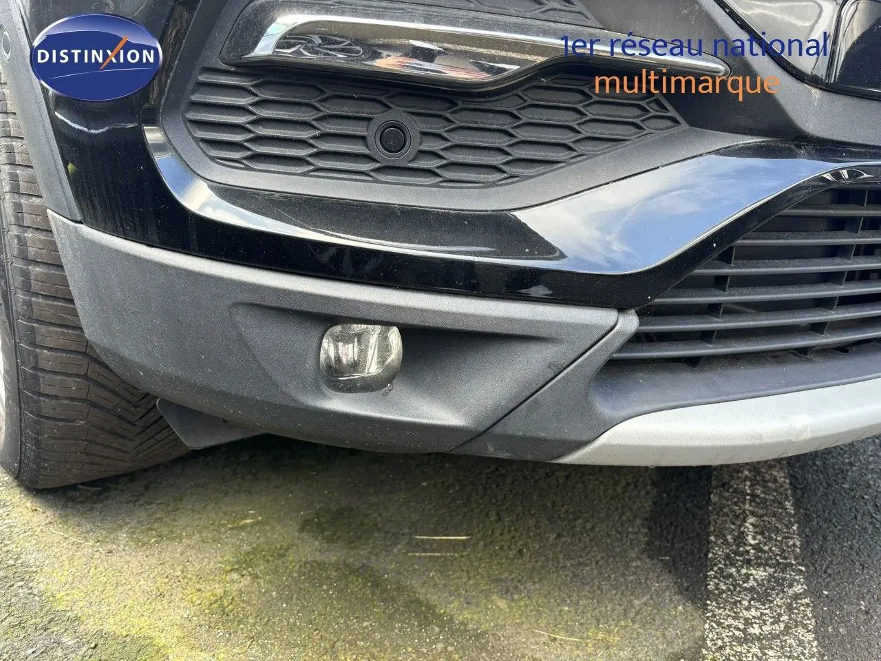 Gros plan sur le pare-chocs avant noir d'un Opel Grandland X 2019, mettant en valeur la calandre et le feu antibrouillard.