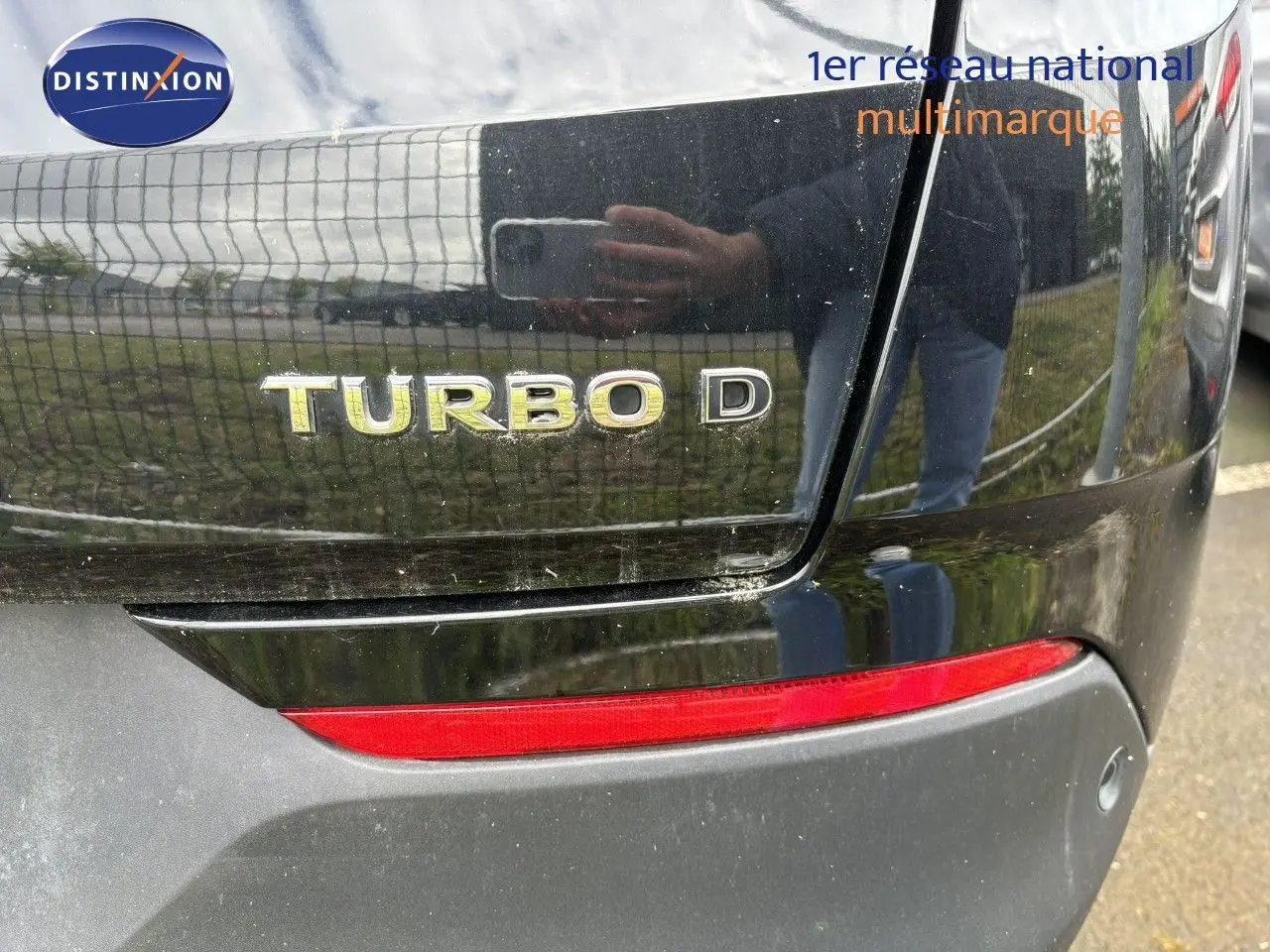 Gros plan sur le logo Turbo D à l'arrière d'un Opel Grandland X noir, avec feu arrière rouge visible.