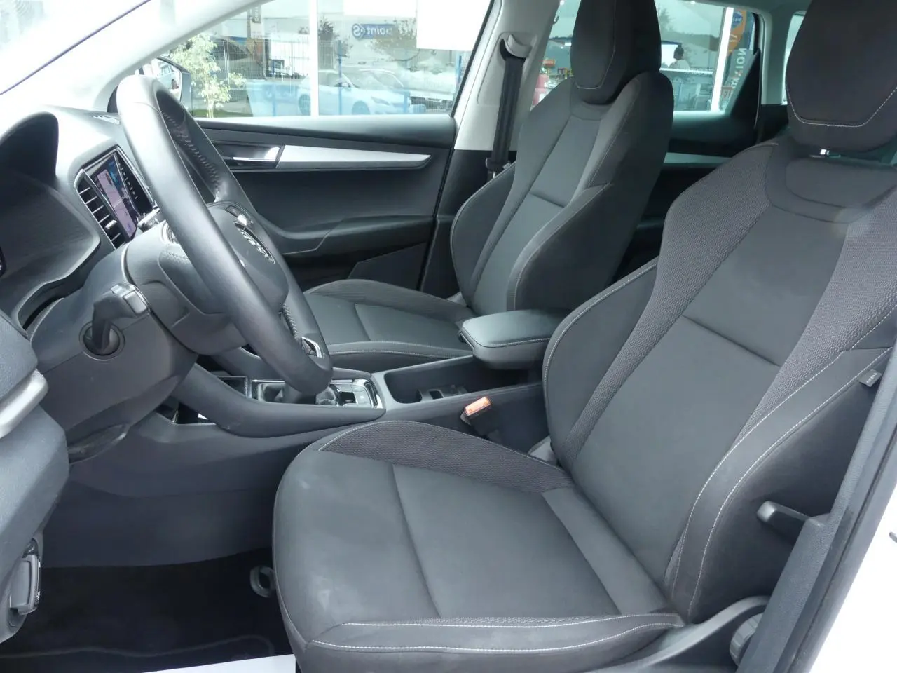Intérieur avant côté conducteur du Skoda Karoq blanc 2024, sièges tissu noir et console centrale avec accoudoir