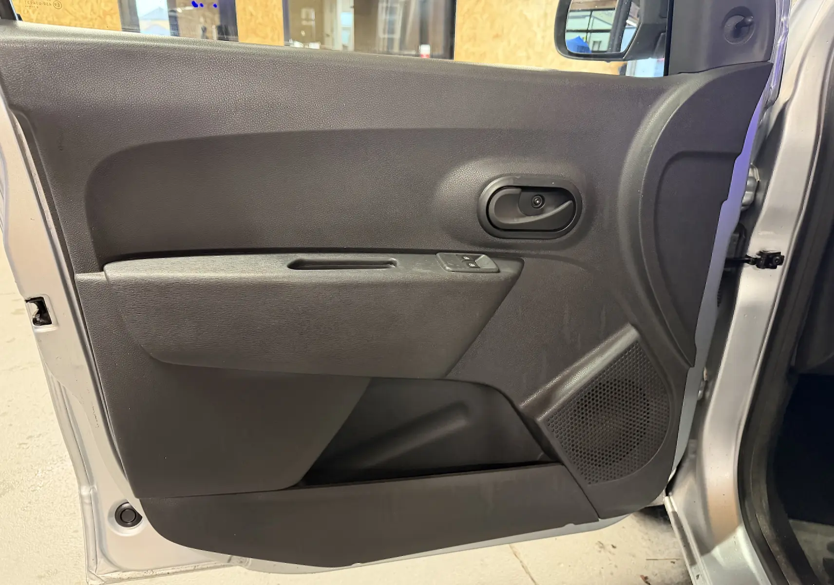 Gros plan sur la porte avant gauche grise d'un Dacia Dokker 2019, avec poignée noire et haut-parleur intégré.
