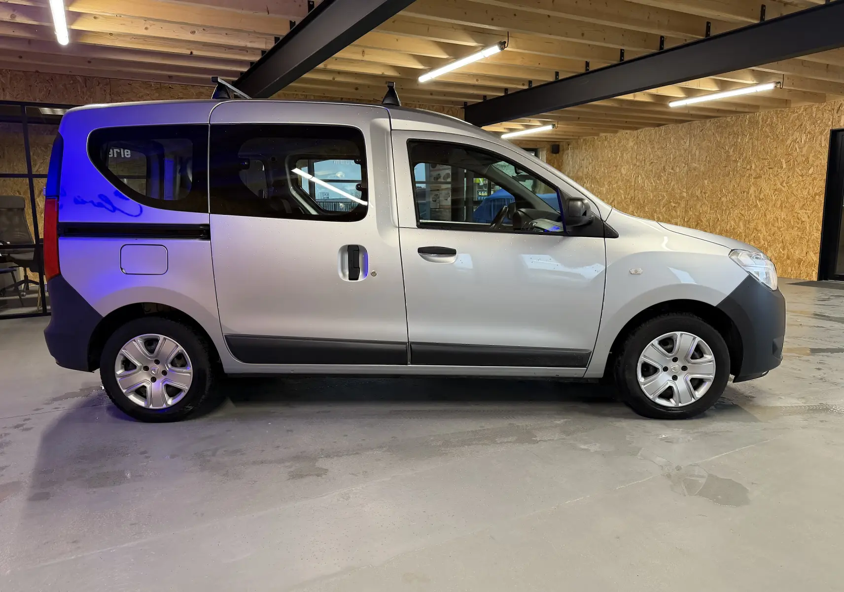 Profil droit d'un Dacia Dokker gris 2019 avec portes coulissantes et jantes en alliage dans un garage éclairé.