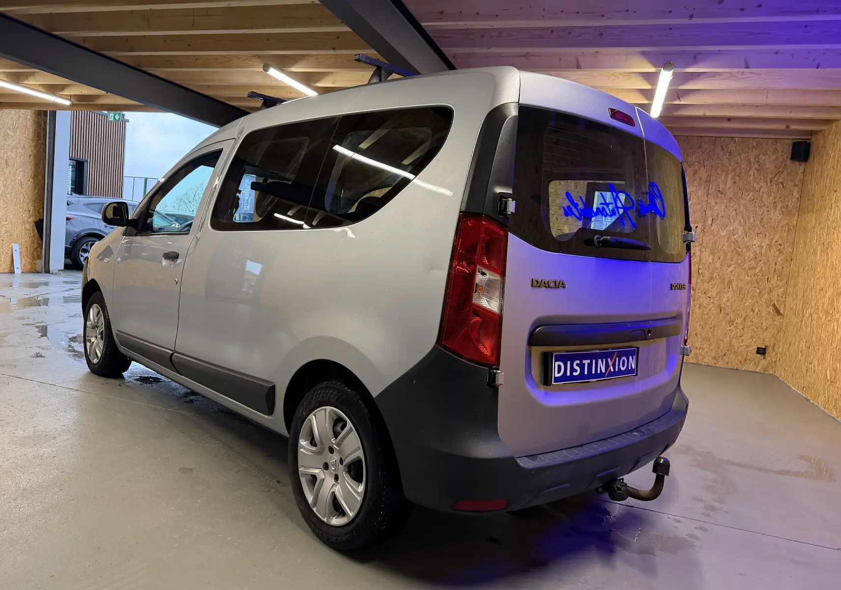 Vue 3/4 arrière droite d'un Dacia Dokker gris 2019 avec hayon, vitres teintées et attelage visible en intérieur.