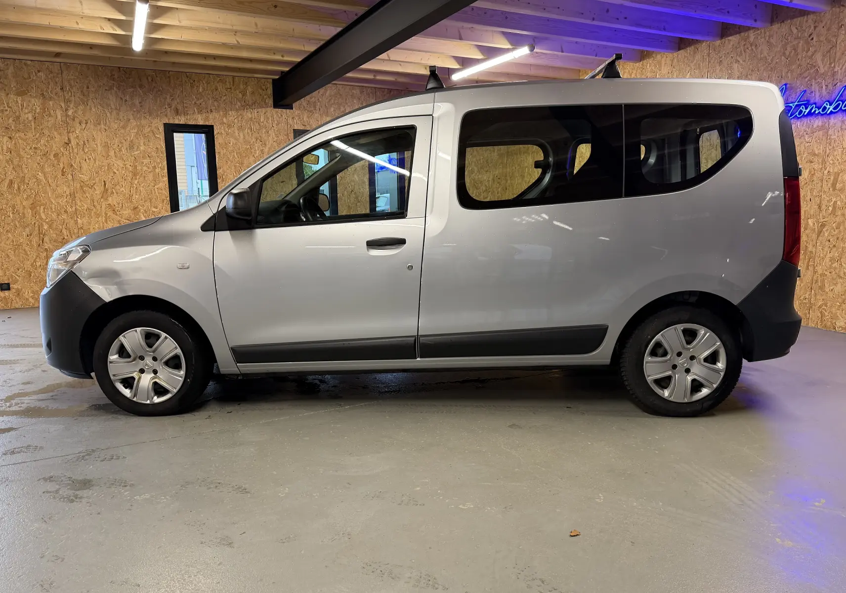 Profil côté gauche d'un Dacia Dokker gris 2019 avec vitres teintées et enjoliveurs dans un garage intérieur.
