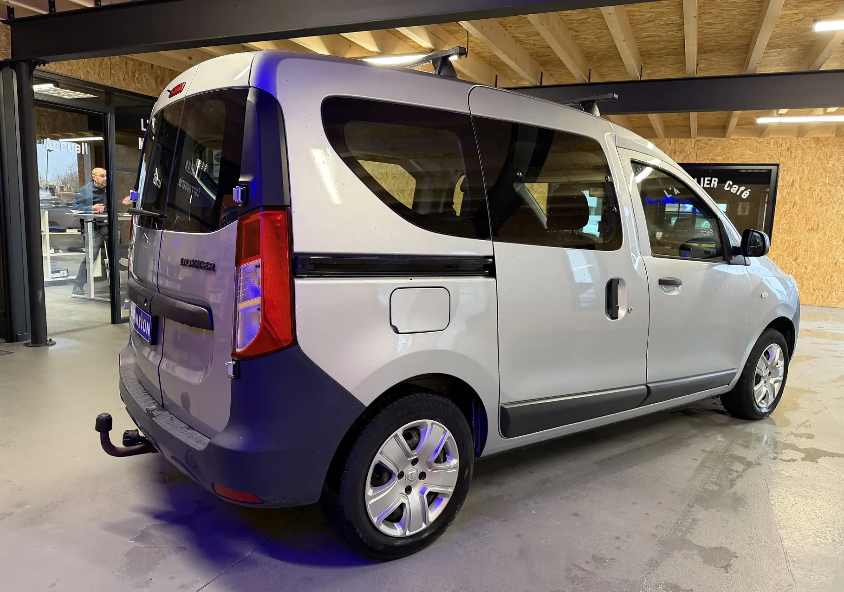 Vue 3/4 arrière droite d'un Dacia Dokker gris 2019 avec attelage et vitres teintées en intérieur showroom.