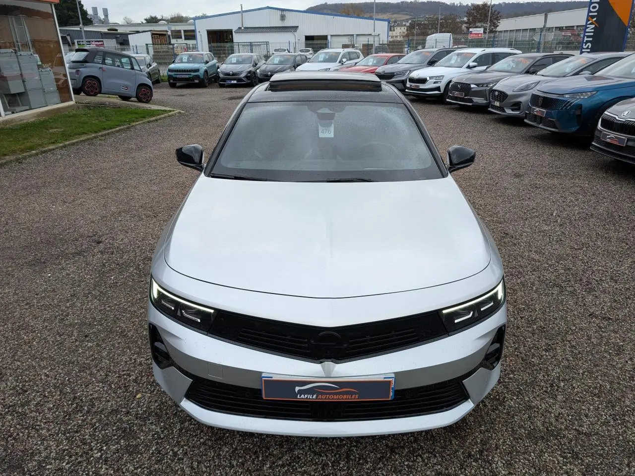 Vue avant d'une Opel Astra 2024 gris métallisé avec toit noir et phares LED allumés sur un parking.