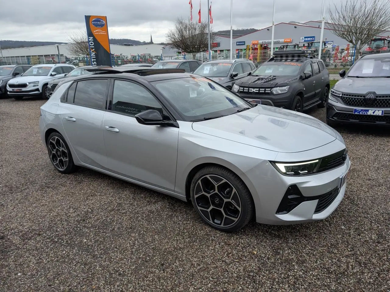 Opel Astra 2024 gris métallisé vue 3/4 avant droit avec toit noir et jantes alliage distinctives.