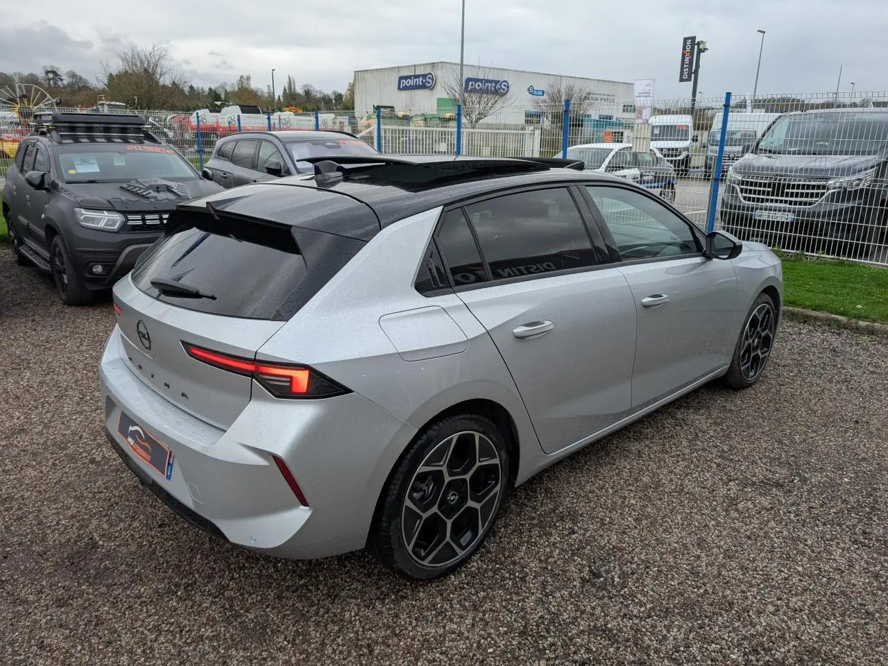 Opel Astra 2024 gris métallisé vue 3/4 arrière droit, toit noir et jantes au design hexagonal distinctif.