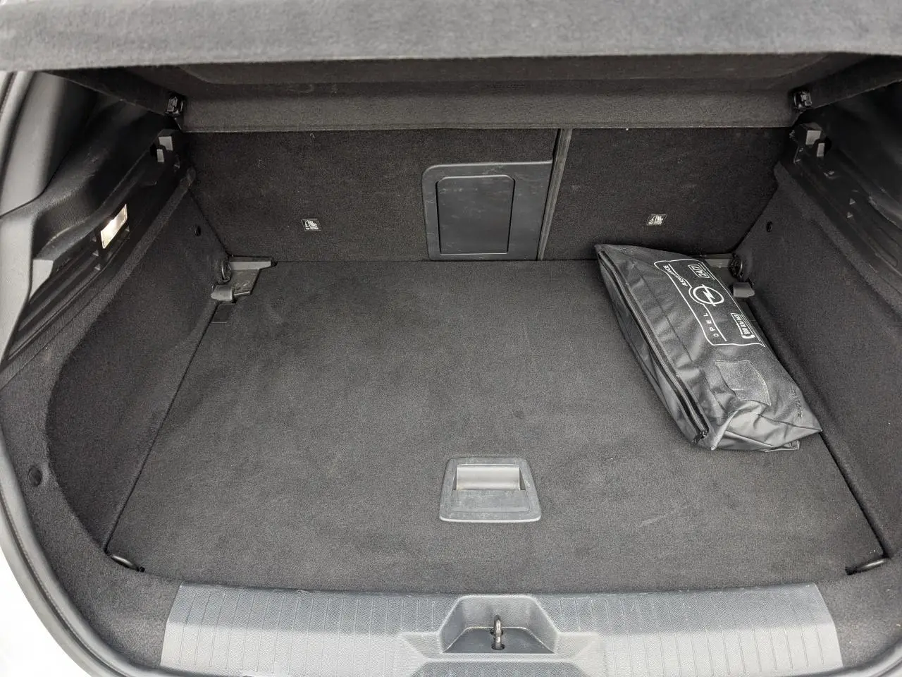 Coffre ouvert d’une Opel Astra 2024 gris métallisé, montrant un espace de rangement avec une trousse de secours noire.