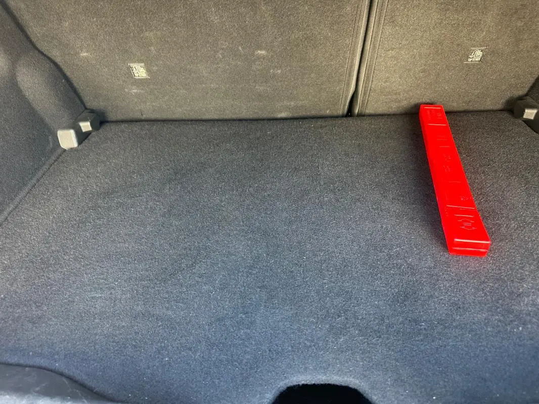Vue rapprochée de la malle arrière du Jeep Avenger 2025, tapis gris foncé avec triangle de signalisation rouge posé dessus.
