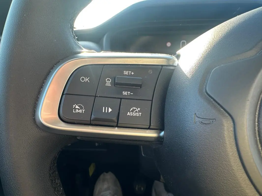 Gros plan sur les commandes à gauche du volant cuir du Jeep Avenger gris foncé, avec boutons de régulateur et limiteur de vitesse.