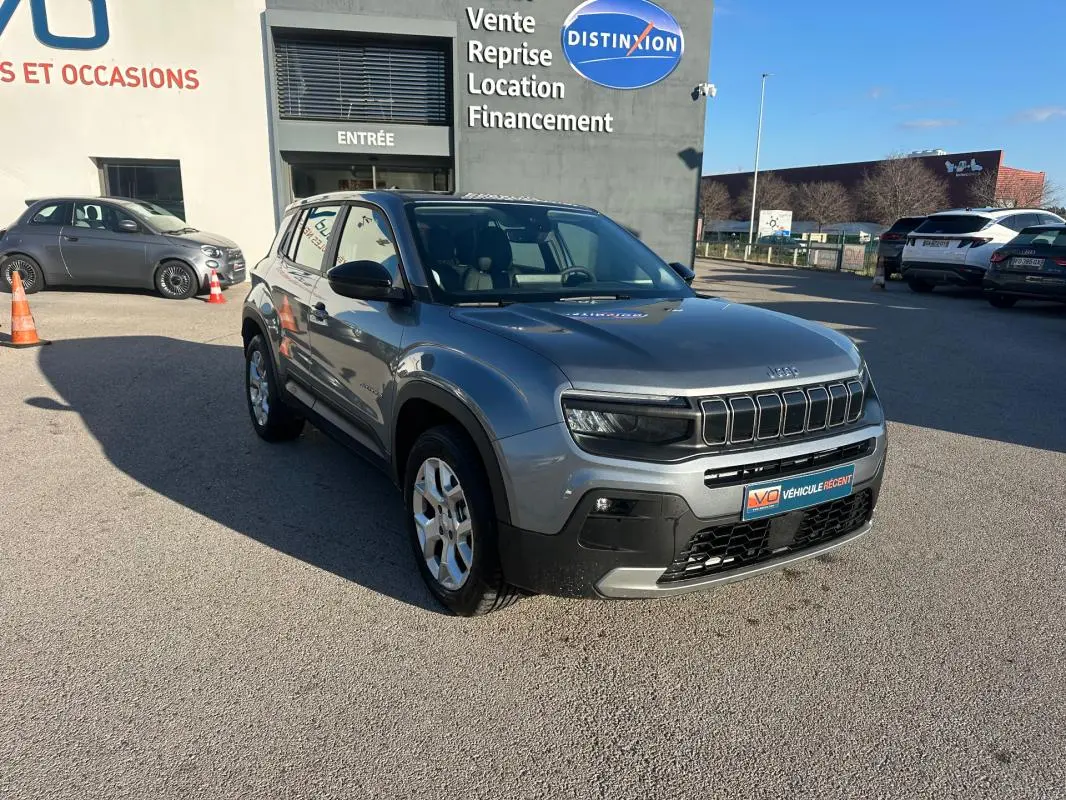 Jeep Avenger gris foncé vue 3/4 avant droit, avec calandre distinctive et jantes alliage 17 pouces, stationné devant un bâtiment.