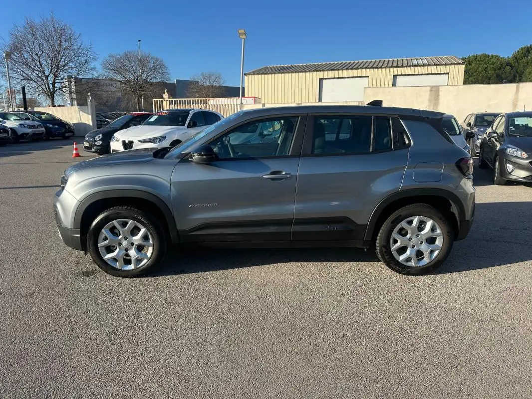 Vue de profil côté gauche d'un Jeep Avenger gris foncé avec jantes alliage 17 pouces sur un parking extérieur.