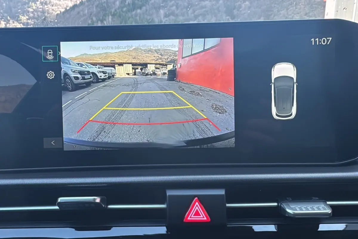 Écran multimédia du Kia Sportage 2026 montrant la caméra de recul avec vue arrière sur un parking et un mur rouge.