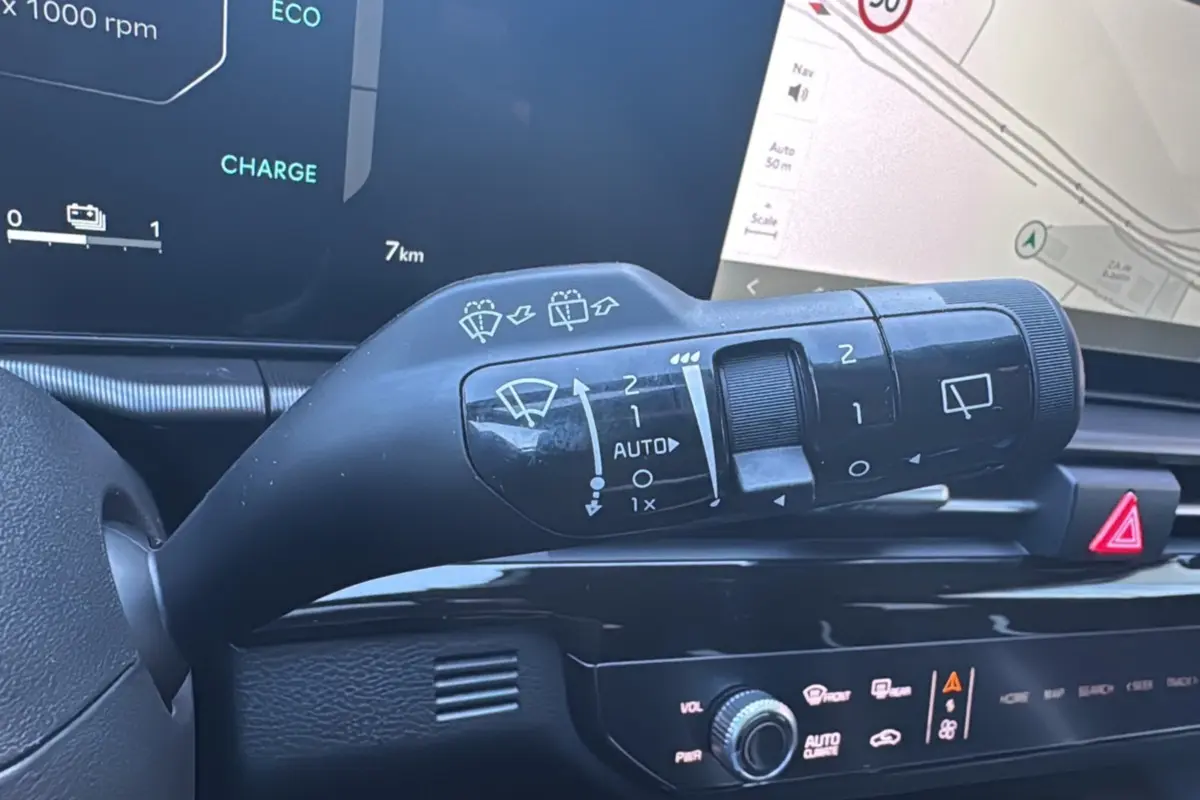 Gros plan sur la commande d’essuie-glace du Kia Sportage noir étoilé, avec écran tactile de navigation en arrière-plan.