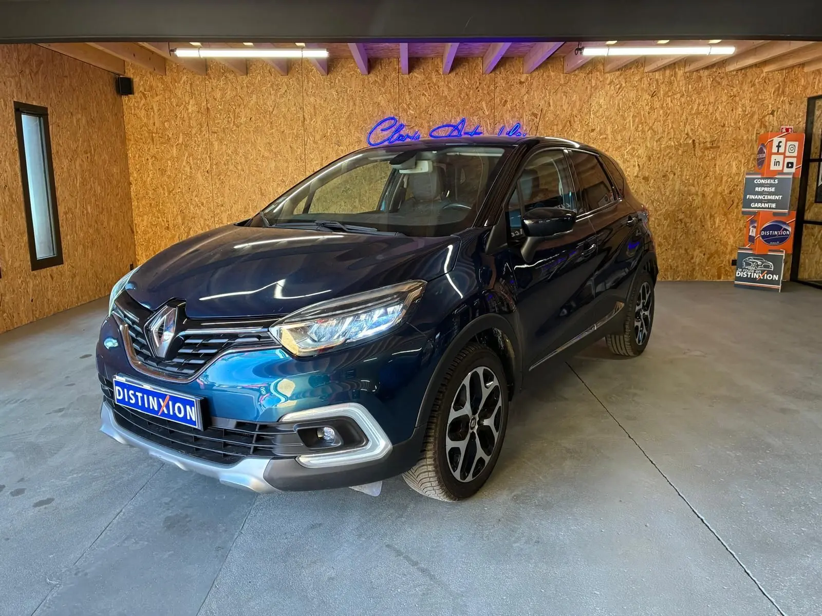 Renault Captur bleu 2017 en 3/4 avant droit, avec jantes alliage et calandre chromée, dans un garage intérieur.
