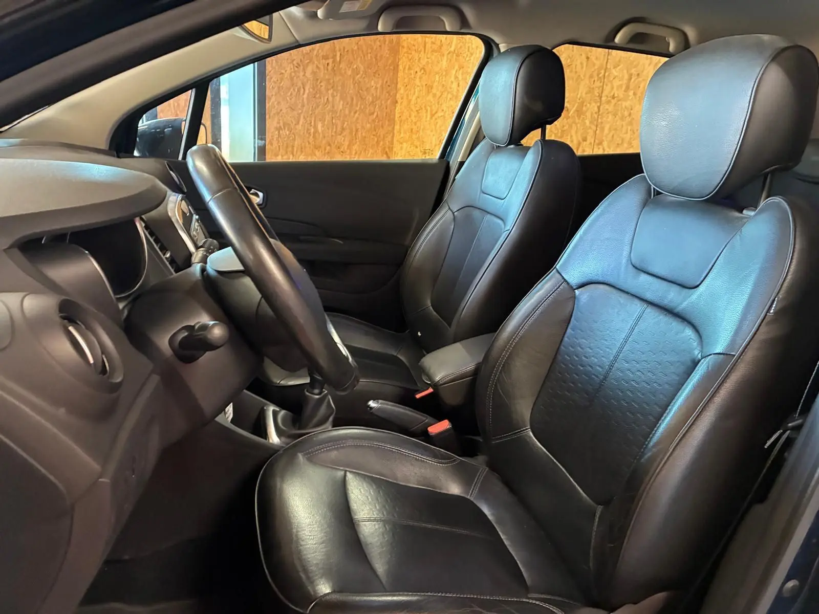 Vue intérieure côté conducteur du Renault Captur bleu 2017, sièges avant en cuir noir avec volant et tableau de bord visibles.