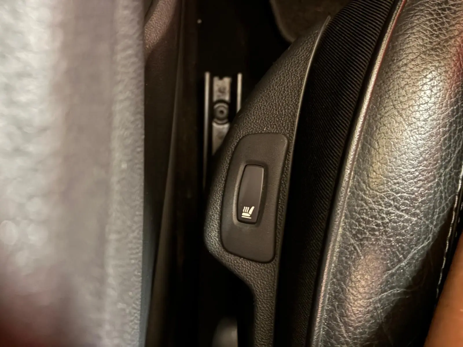 Gros plan sur le bouton de siège chauffant noir dans l'habitacle du Renault Captur 1.5 DCI 90 Intens.