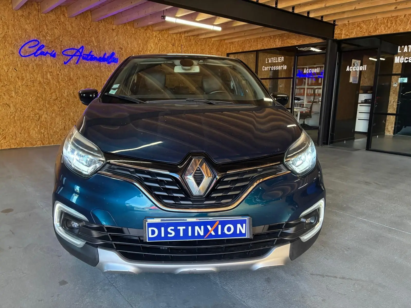 Vue de face du Renault Captur bleu 2017 avec calandre noire et plaque Distinxion dans un garage intérieur.