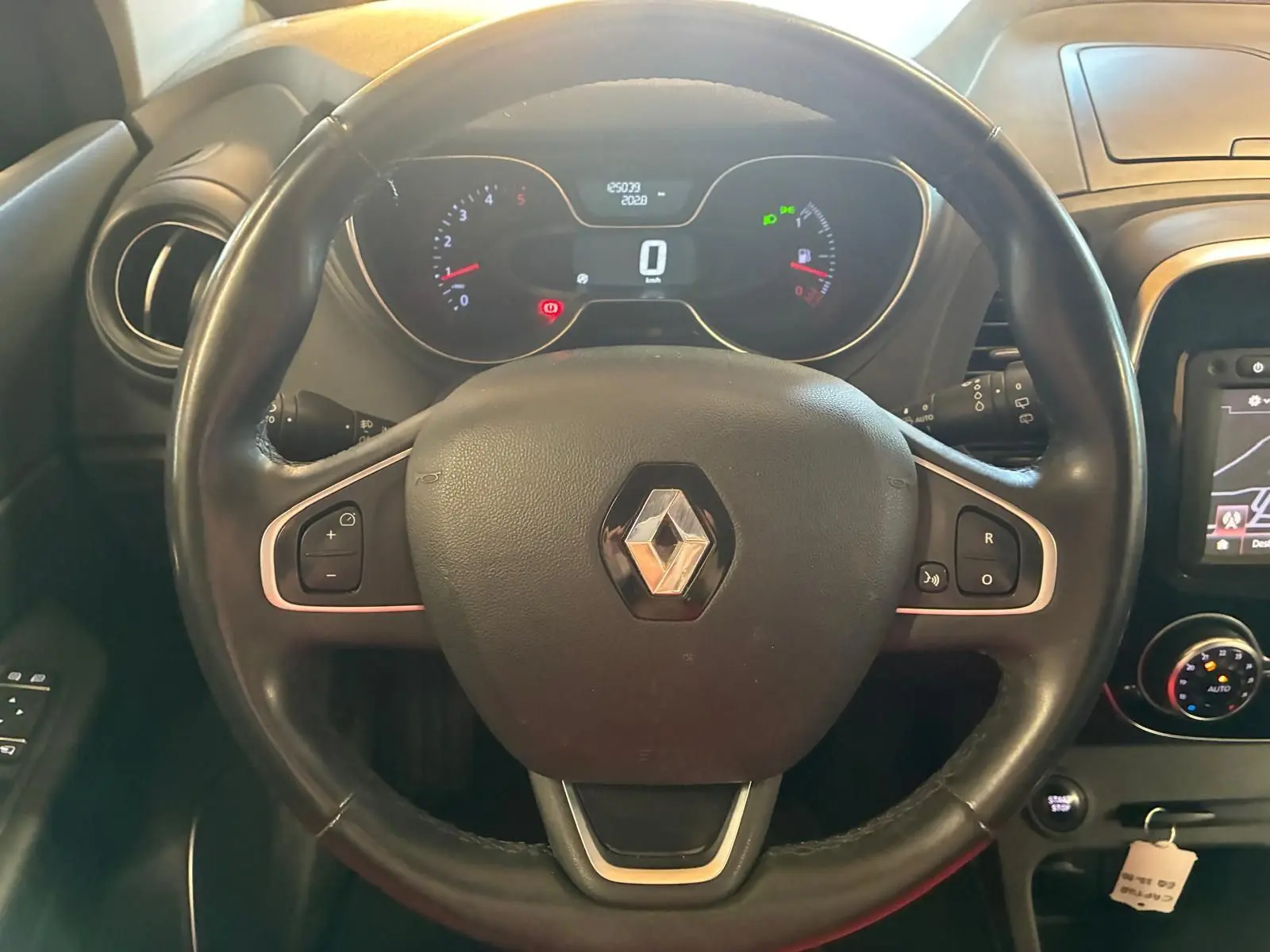 Vue intérieure centrée sur le volant noir avec logo Renault, tableau de bord numérique et commandes intégrées visibles.