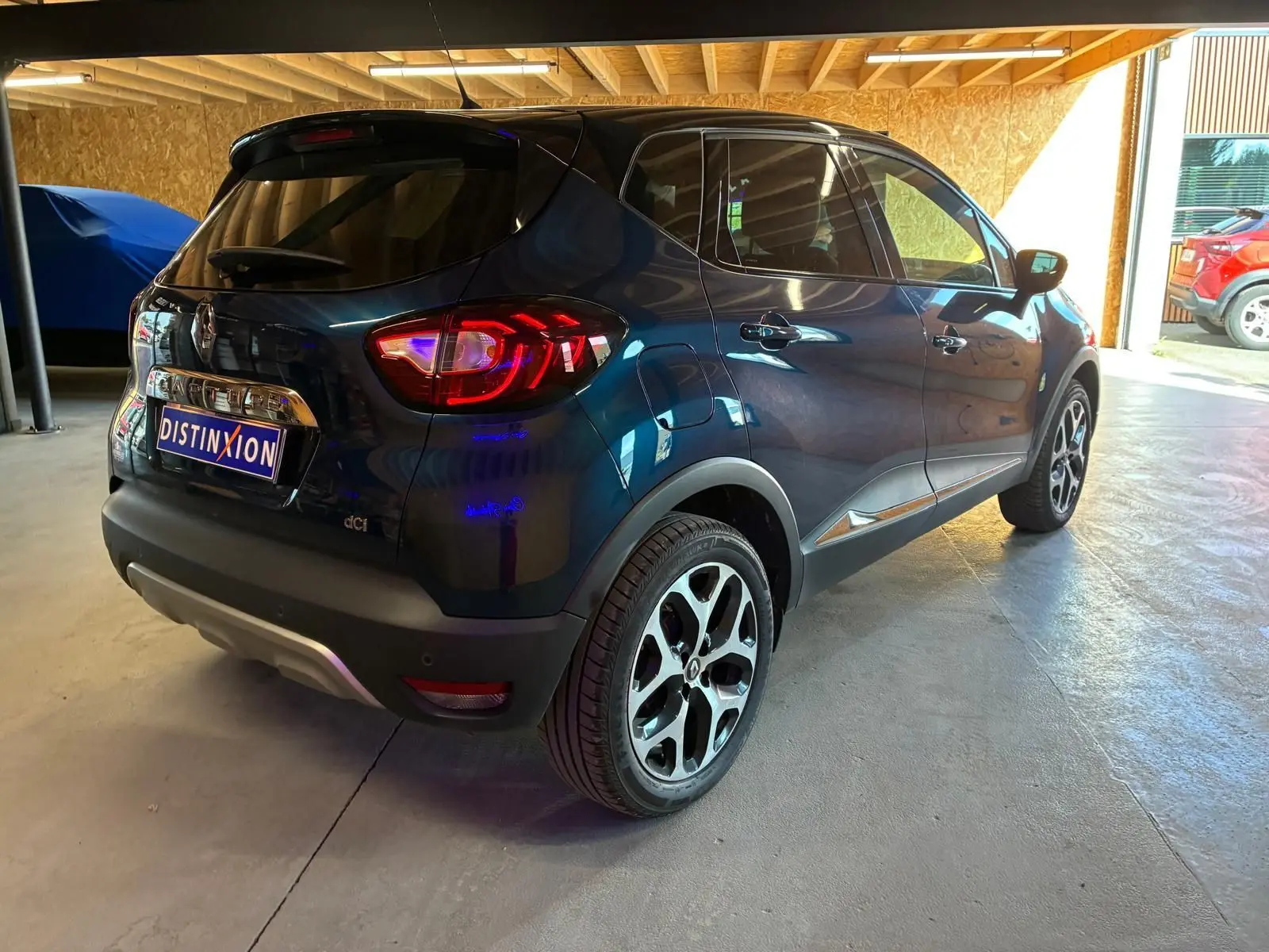 Vue 3/4 arrière droite d’un Renault Captur bleu 2017 avec jantes alliage et feux arrière allumés en intérieur.