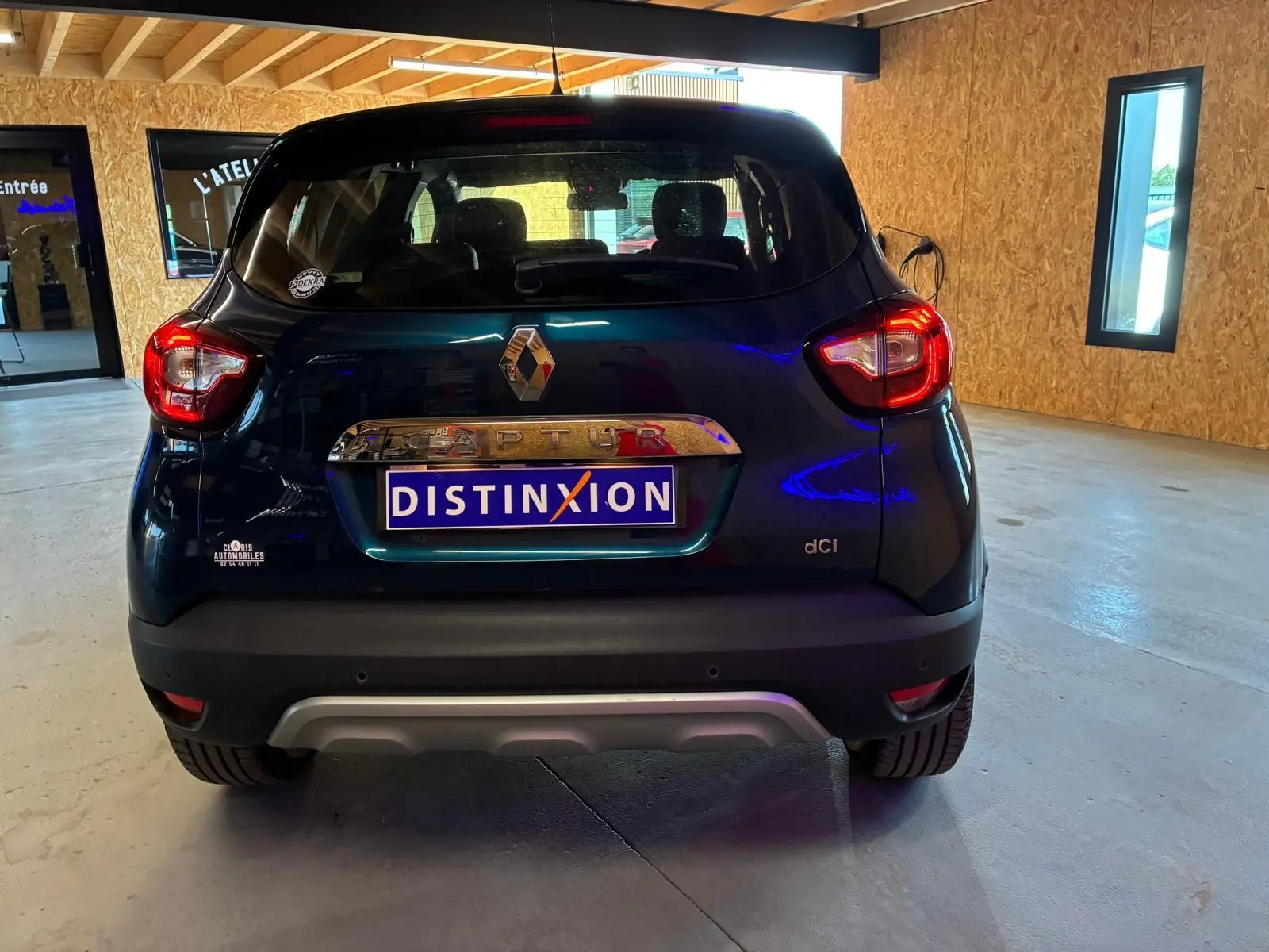 Vue arrière d'un Renault Captur bleu 2017 avec logo et plaque Distinxion dans un garage lumineux.