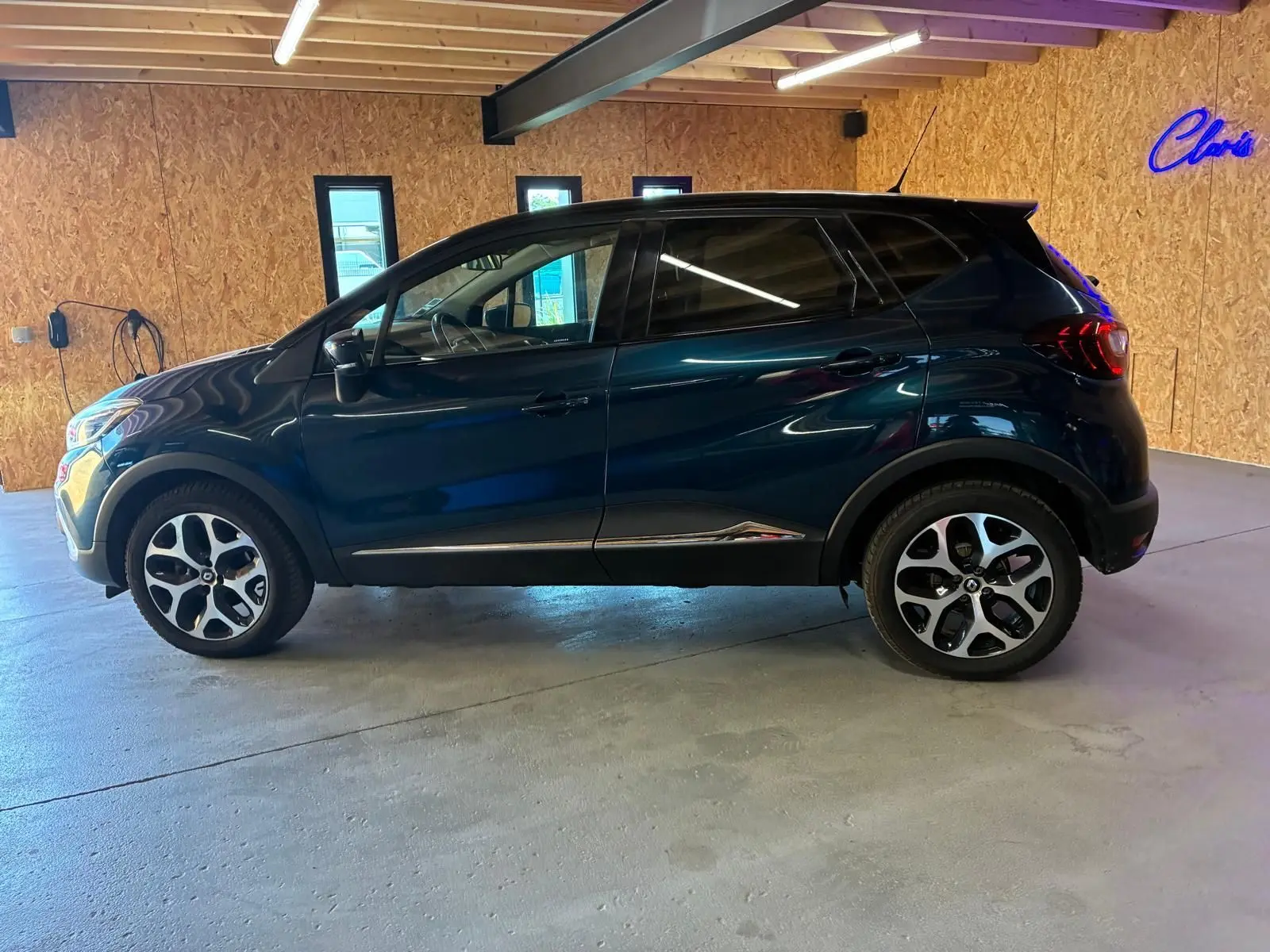 Vue de profil côté gauche d'un Renault Captur bleu 2017 garé en intérieur avec jantes alliage distinctives.