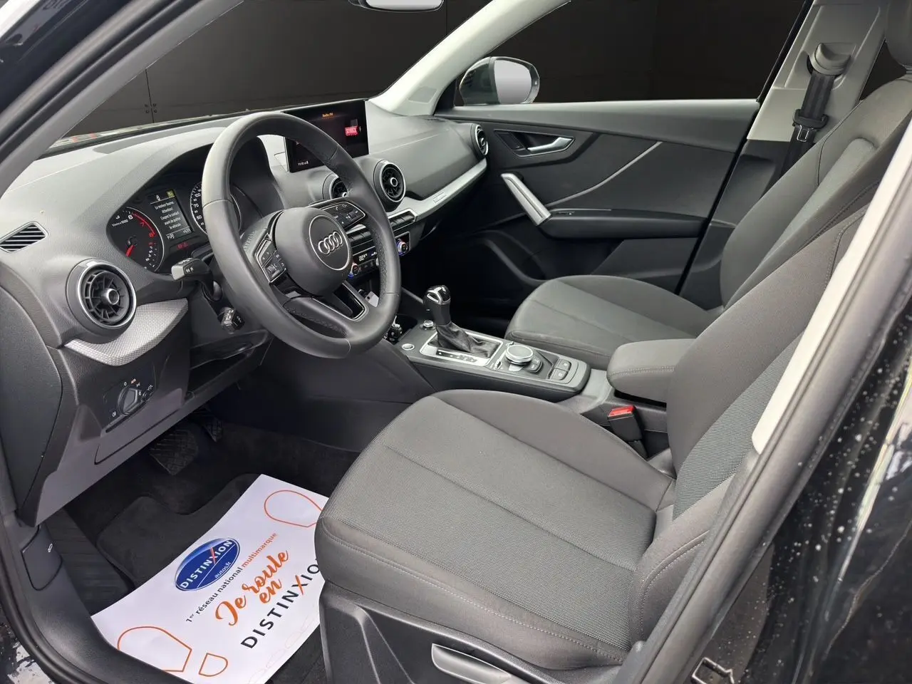 Intérieur avant droit d'Audi Q2 noir Mito 2023, sièges tissu gris, volant multifonction et console centrale avec levier automatique.