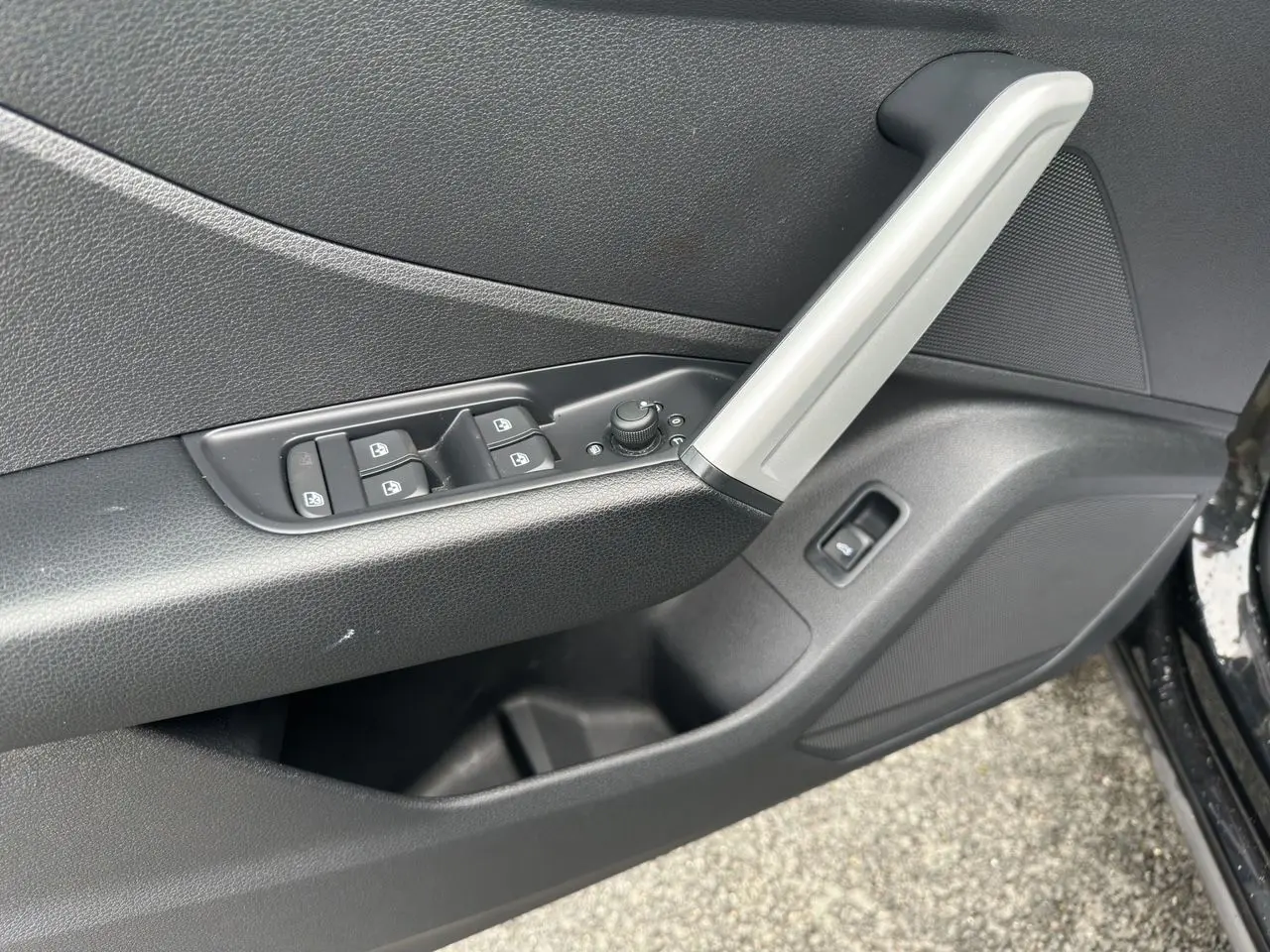 Gros plan sur la porte avant gauche noire de l'Audi Q2 2023, avec commandes des vitres et poignée argentée.