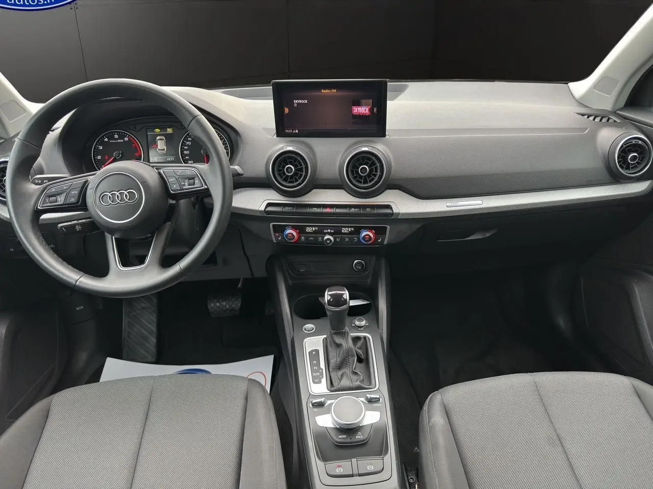 Vue intérieure avant de l'Audi Q2 35 TFSI S-Line 2023, tableau de bord noir avec écran central et commandes MMI visibles.
