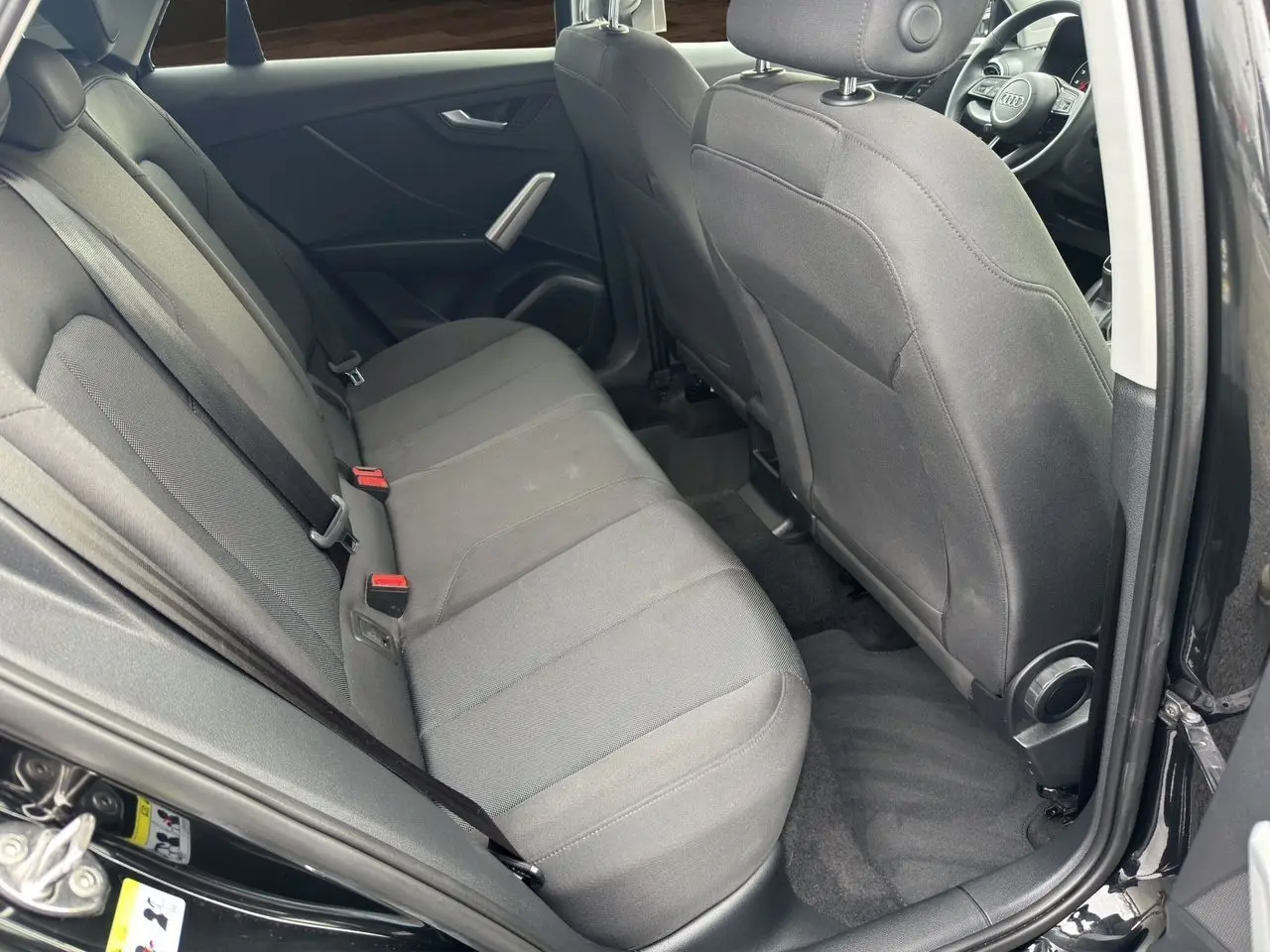 Vue intérieure côté arrière droit de l'Audi Q2 noir mito, montrant les sièges arrière en tissu et la porte ouverte.