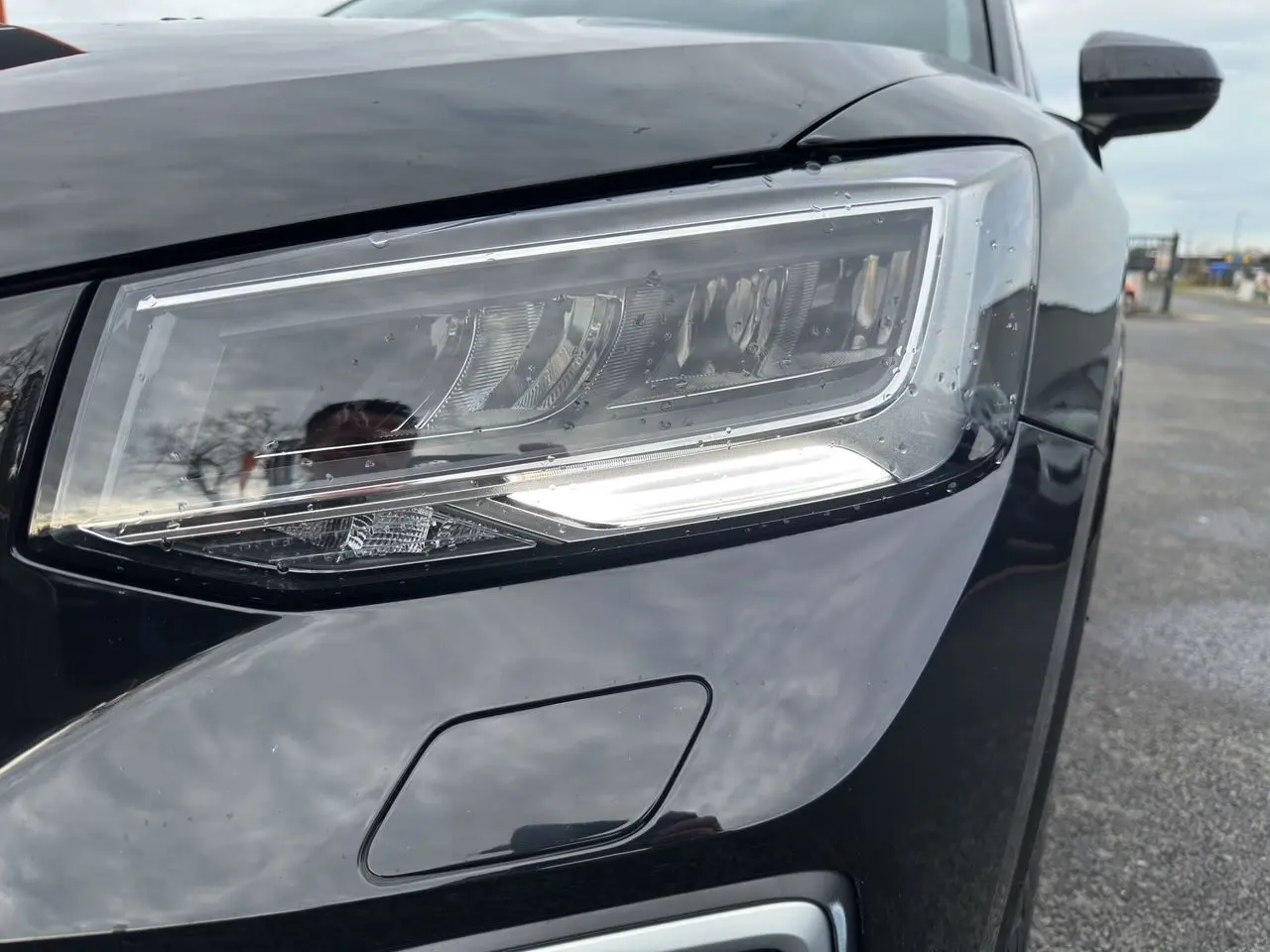 Gros plan sur le phare avant droit noir mito de l'Audi Q2 35 TFSI S-Line 2023 avec éclairage LED et capteur de lavage.