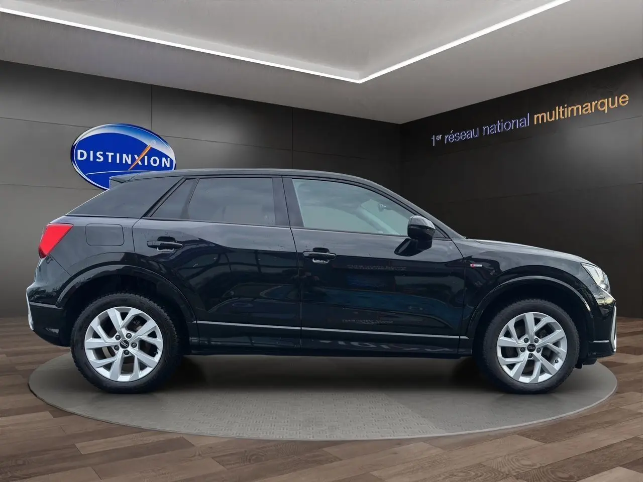 Audi Q2 noir mito vue de profil côté gauche, avec jantes alliage 7x17 et hayon motorisé visible en arrière-plan.