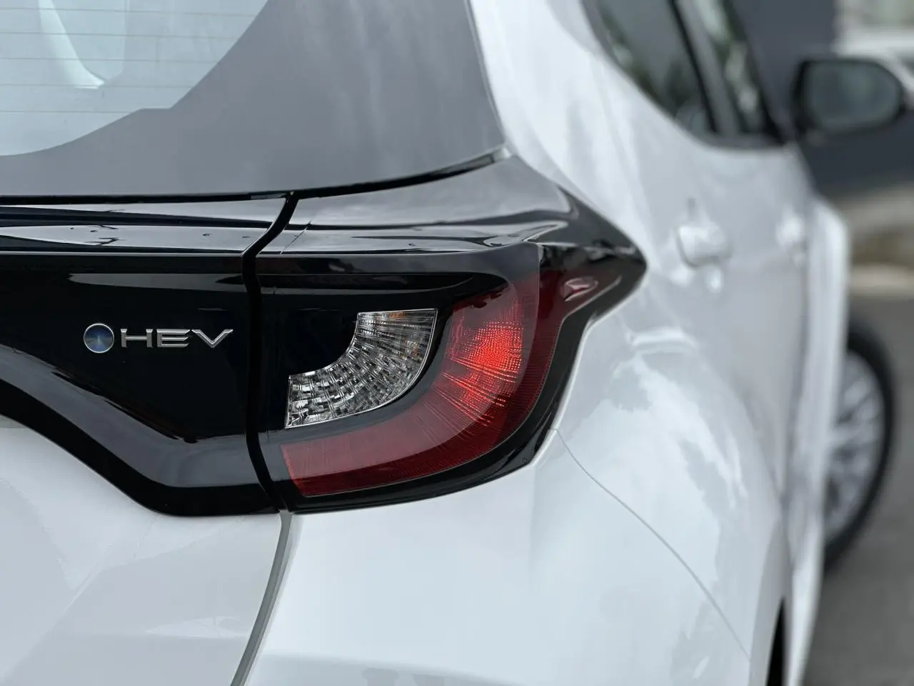 Gros plan sur le feu arrière gauche noir et blanc pur de la Toyota Yaris Hybride 2025 avec logo HEV visible.