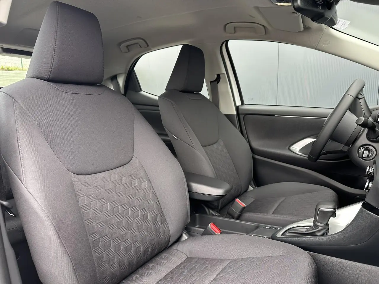 Intérieur de la Toyota Yaris Hybride 2025 montrant les sièges tissu noir et accoudoir central côté conducteur.