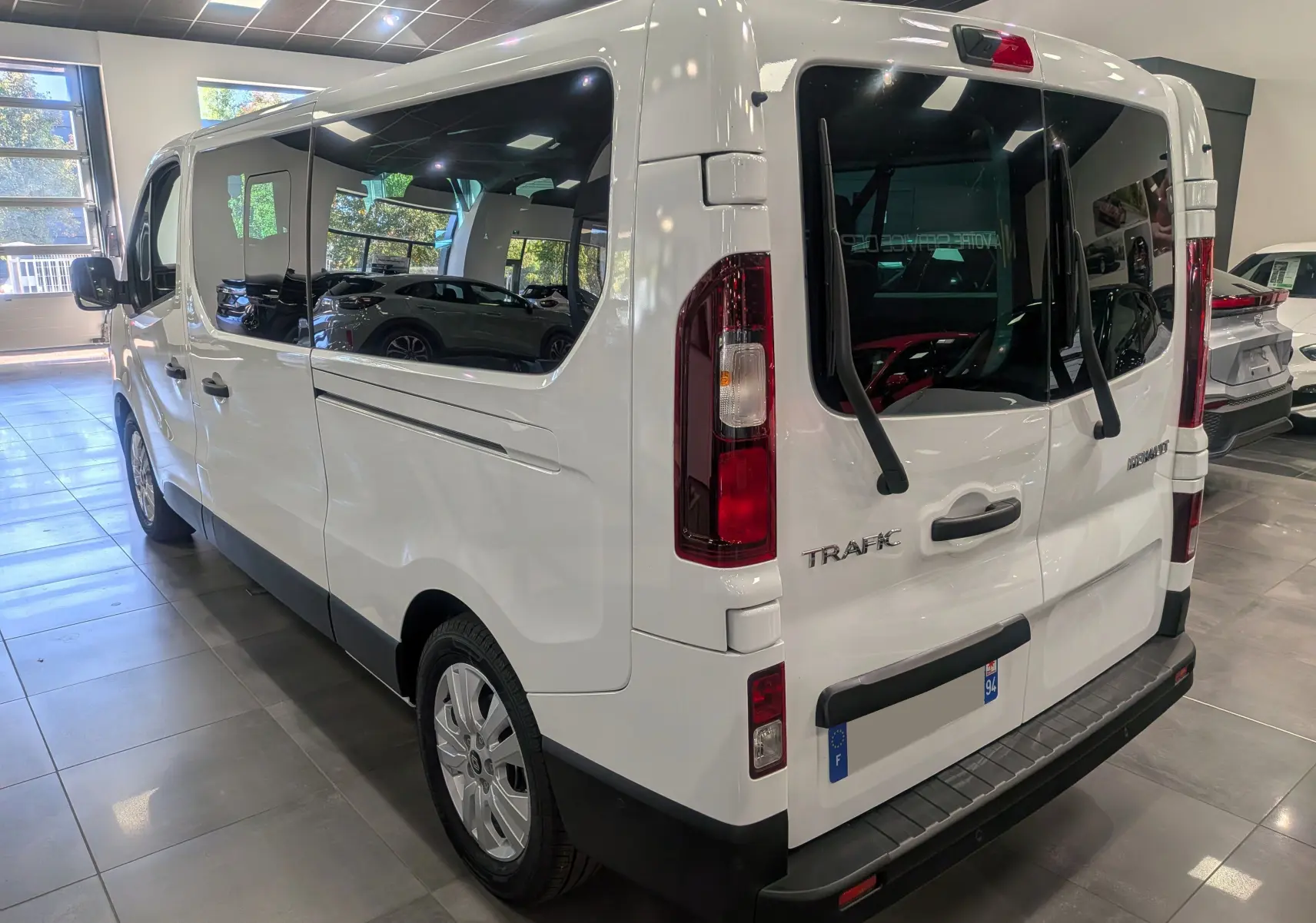 Vue 3/4 arrière droite du Renault Trafic Combi blanc glacier, soulignant ses grandes vitres latérales et hayon arrière.