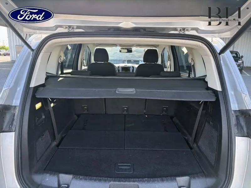 Vue arrière du coffre ouvert du Ford S-MAX gris lunaire avec banquette arrière rabattue et cache-bagages déployé.