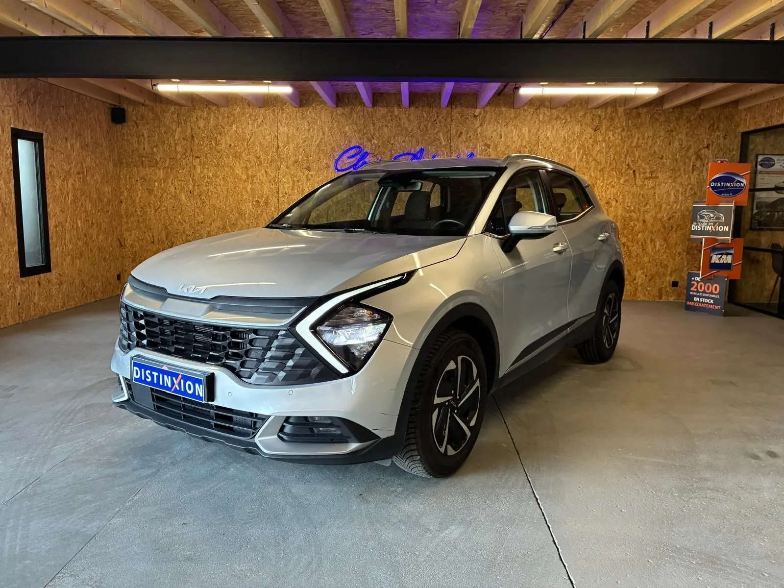 KIA Sportage hybride gris 2024 vu en 3/4 avant droit, avec calandre noire et jantes distinctives.