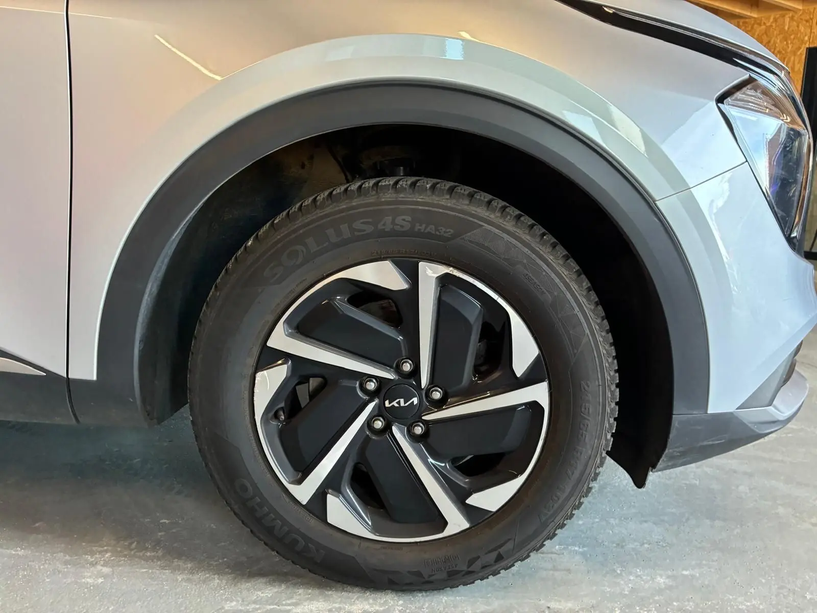 Gros plan sur la roue avant droite d’un Kia Sportage gris 2024, mettant en valeur la jante alliage bicolore au design moderne.