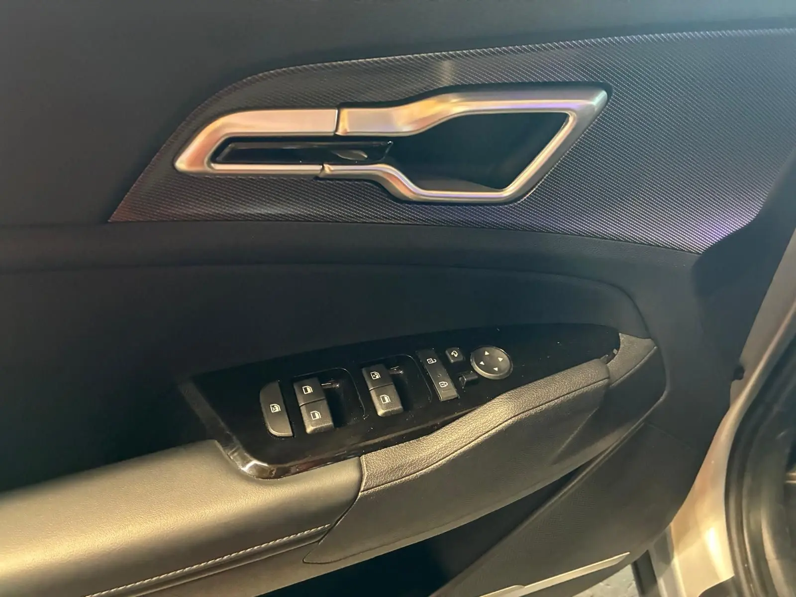 Poignée de porte intérieure et commandes des vitres côté conducteur du KIA Sportage gris hybride 2024, vue rapprochée.