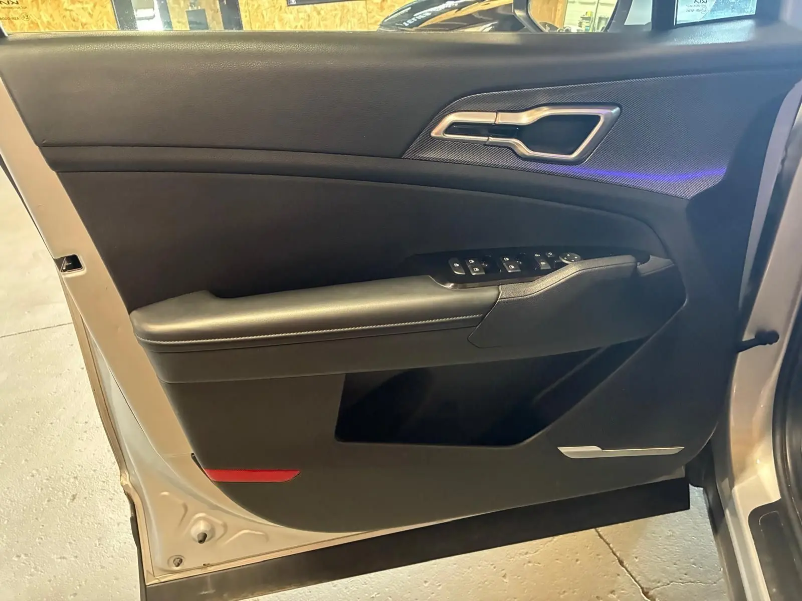 Vue intérieure sur la porte avant gauche du Kia Sportage gris 2024, avec commandes de vitres et poignée métallique.