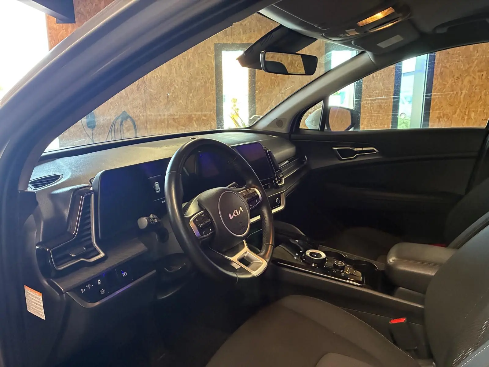 Intérieur du Kia Sportage 2024 hybride en vue côté conducteur, avec tableau de bord noir et volant multifonction.