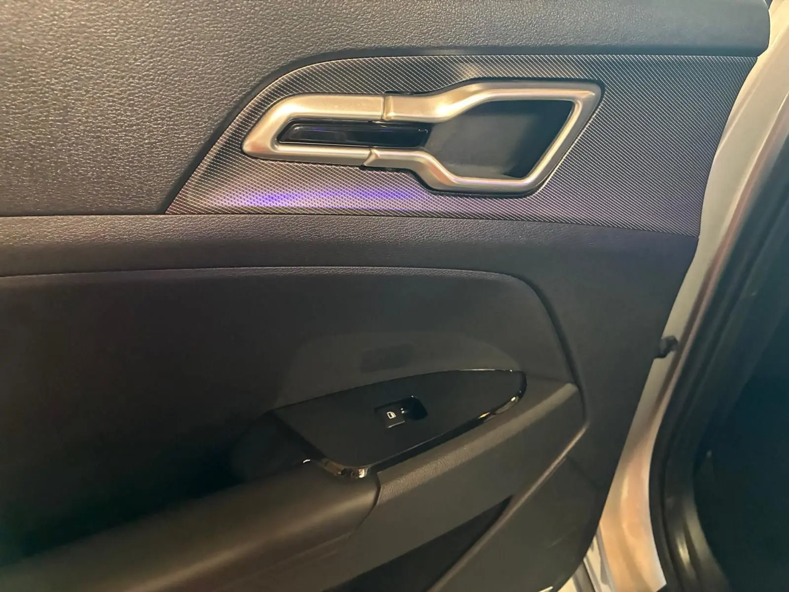 Détail de la poignée intérieure et commande de vitre sur la porte avant gauche d’un Kia Sportage gris 2024.