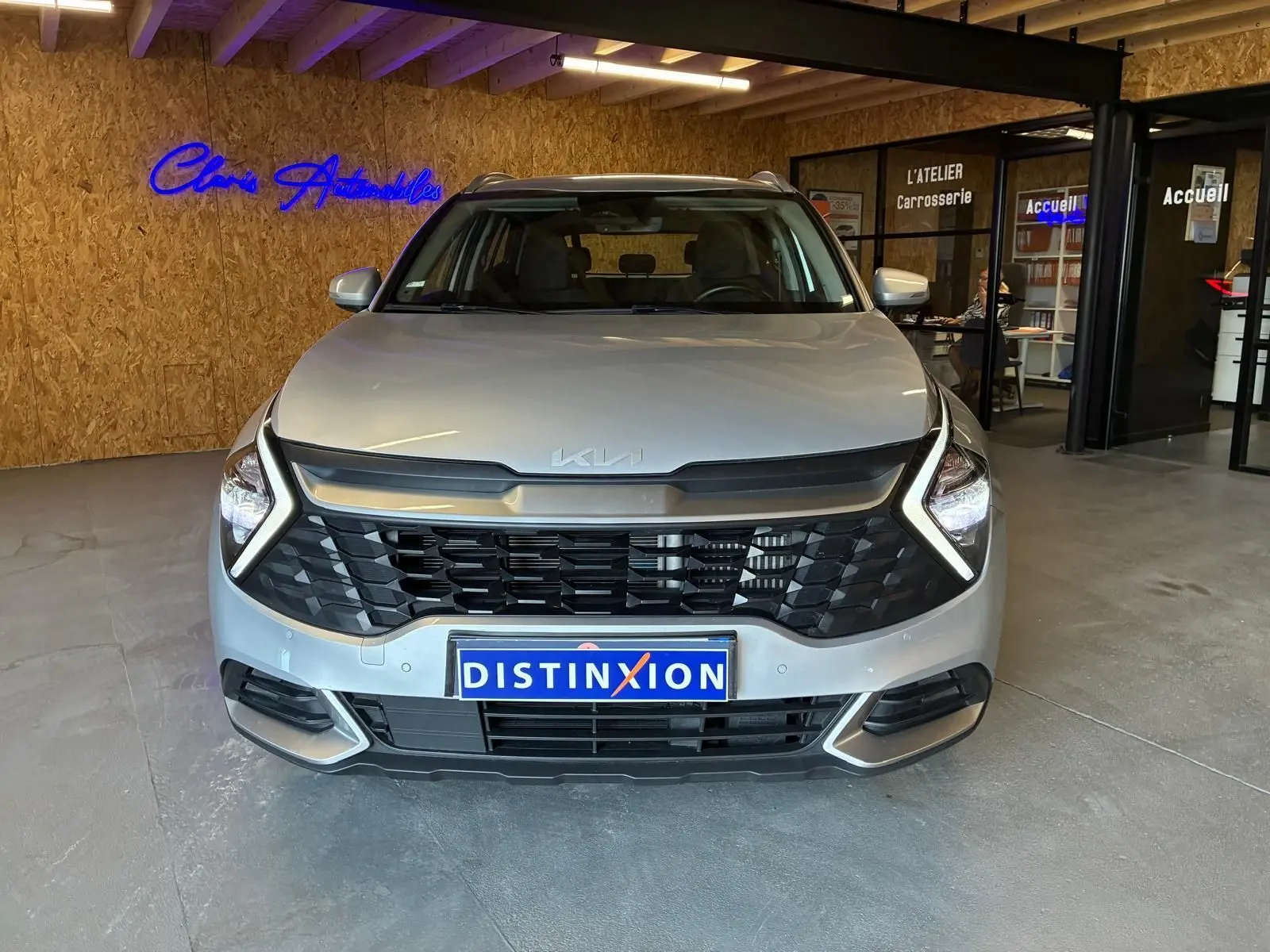 Vue frontale du KIA Sportage gris 2024 hybride avec calandre noire et éclairage LED en forme de boomerang.